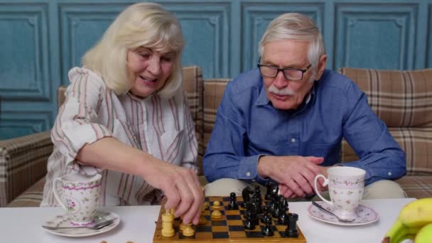 Starší pár v důchodu mluví o pití čaje, hraje šachy v moderním obývacím pokoji salonek spolu — Stock video
