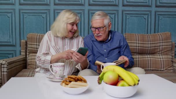 Ηλικιωμένοι παππούδες μιλάνε και χρησιμοποιούν ψηφιακό κινητό τηλέφωνο στο σπίτι. Online αγορές — Αρχείο Βίντεο