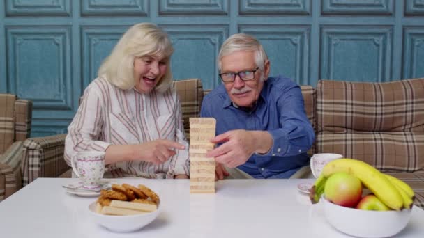 Пенсионеры проводят время вместе, играя в игру с деревянными блоками на столе в гостиной — стоковое видео