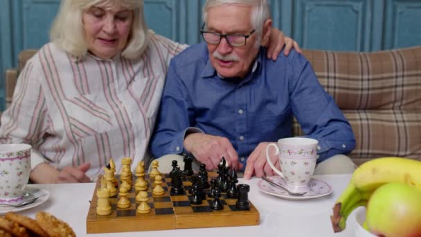 Pensionato coppia anziana parlando di bere il tè, giocando a scacchi nella moderna sala salotto casa insieme — Video Stock