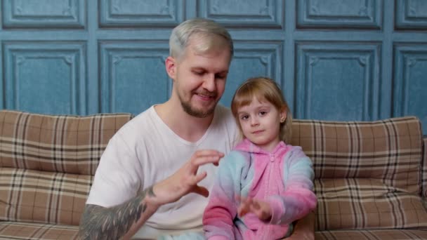 Père et enfant fille enfant en pyjama assis sur le canapé souriant, faisant signe de la forme coeur près de la poitrine — Video