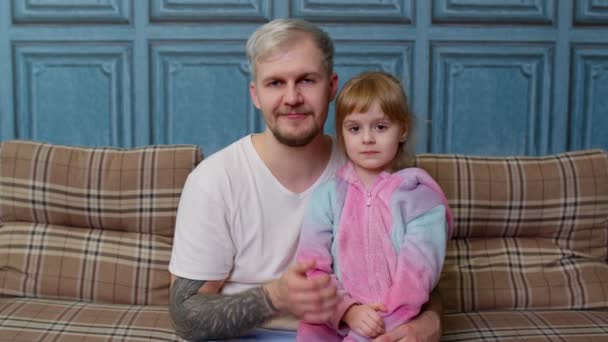 Far og barn datter pige i pyjamas sidde på sofaen i rummet smilende, blæser sende et luftkys – Stock-video
