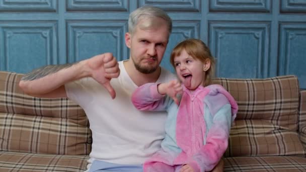 Utilfreds far og barn datter barn i pyjamas sidde på sofaen i rummet, viser tommelfinger ned modvilje – Stock-video