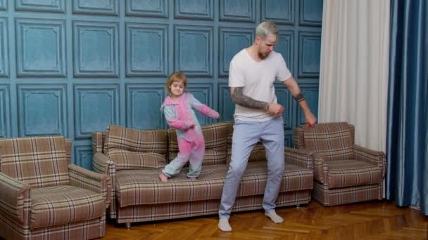 Ung far babysiter och liten dotter hoppar dans på soffan i modernt hus vardagsrum — Stockvideo