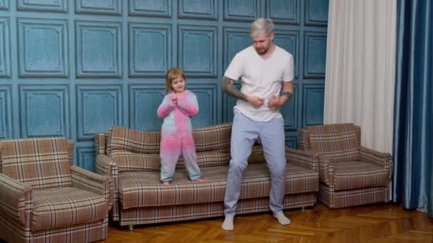 Feliz família engraçada pai e criança criança filha dançando, pulando no sofá, ouvindo música em casa — Vídeo de Stock