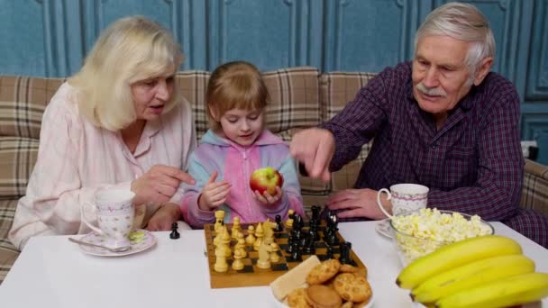 Senior couple grandfather, grandmother resting on sofa, playing chess with granddaughter child kid — Stock Video