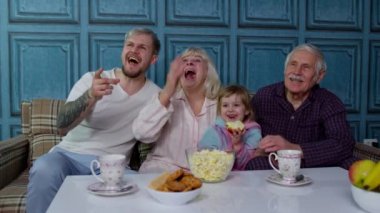 Çoklu mutlu aile gülüyor, çizgi film izliyor, evde patlamış mısır yiyor.