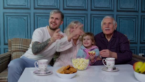 Familia multigeneracional ver la televisión con el niño joven en casa, riendo mientras ve la película de dibujos animados — Vídeo de stock