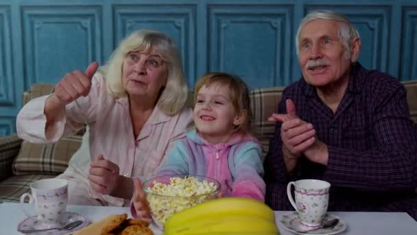 Büyükbabam ve büyükannem mutlu bir şekilde gülüyor, patlamış mısır yiyor, evde çizgi film seyrediyor. — Stok video