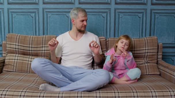 Far og lille datter barn mediterer mens du sidder i yoga lotus udgør på sofaen derhjemme værelse – Stock-video