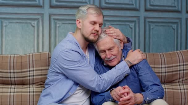 Mladý muž, který se omlouvá vystresovanému staršímu otci sedícímu spolu na gauči — Stock video