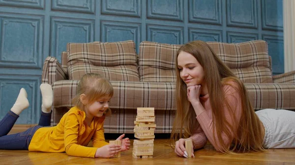 Mother play wooden blocks board game with little daughter child girl at home, leisure hobbies