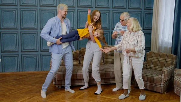 Family members of different generations having fun listening music, dancing crazy in room at home