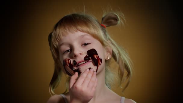 Portré tini mosolygós gyerek gyerek lány elmossa arcát olvadt csokoládé és mutatja hüvelykujj fel jel — Stock videók