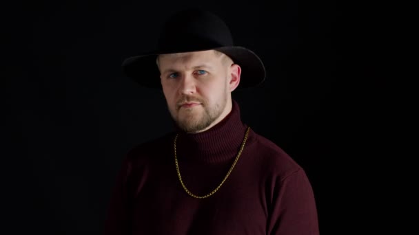 Portret uwodzicielskiego uśmiechniętego młodzieńca w modnych stylowych ubraniach i kapeluszu na czarnym tle — Wideo stockowe