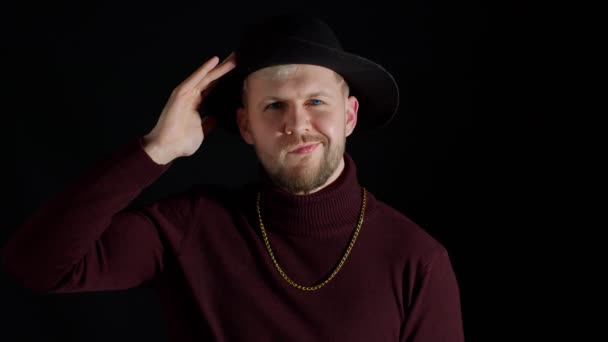 Arckifejezése jóképű férfi elegáns kalap néz kamera és mosolygós fekete háttér — Stock videók
