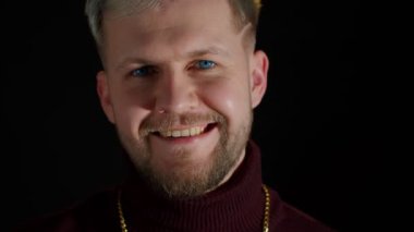 Şık genç adam kameraya bakıyor, mutluluğu, eğlenceyi ve keyfi hissediyor, gülümseme hareketi gösteriyor.