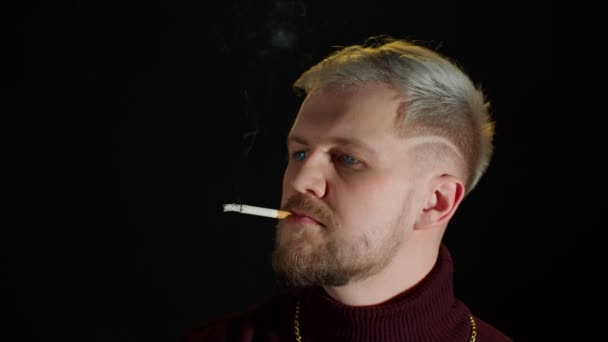 Stylish addicted young man with blue eyes in trendy clothes looking at camera, smoking cigarette — Stock Video