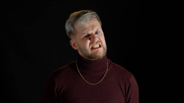 Siyah arka planda olumsuz ve saldırgan duygular gösteren mavi gözlü, hayal kırıklığına uğramış yakışıklı bir adam.