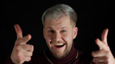 Mutlu, stil sahibi genç adam heyecanlı bir şekilde gülümsüyor ve kamerayı işaret ediyor. Güzellik kazanan talihliyi seçiyor.