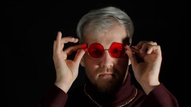 Güneş gözlüğü takan baştan çıkarıcı genç adam, büyüleyici gülümseme göz kırpma, siyah arka planda flört etme.