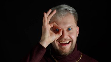 Neşeli heyecanlı genç adam kameraya bakıyor büyüleyici gülüşü gösteriyor Tamam jest, eğlence, keyif