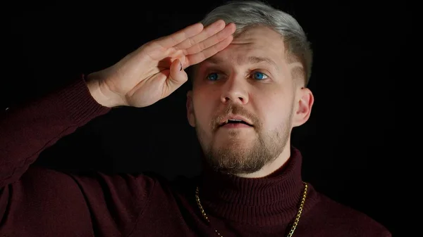 Man in stylish blouse looks around with his hand on his forehead, waving hand hi hello welcome bye