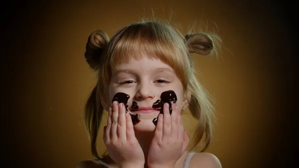 Genç bir çocuğun portresi erimiş siyah çikolatayla yüzünü boyar ve çikolata yemeye başlar.