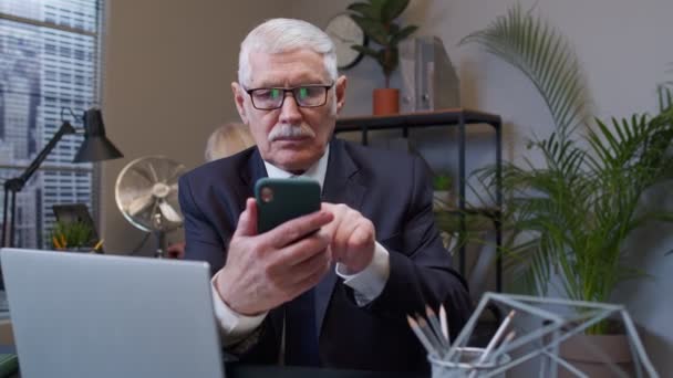Senior Geschäftsmann Großvater mit Smartphone SMS checken E-Mail-Nachrichten online bei der Arbeit — Stockvideo