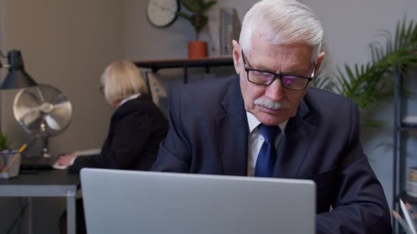 Enfocado empresario senior hombre de negocios escribiendo en el ordenador portátil haciendo investigación, sentado en el escritorio de la oficina — Vídeo de stock