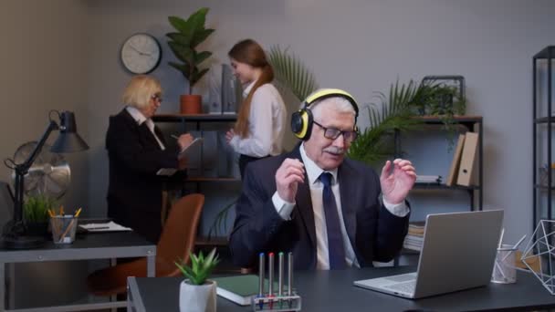 Счастливый старший бизнесмен предприниматель, работающий на ноутбуке, слушающий музыку на наушниках и танцующий — стоковое видео