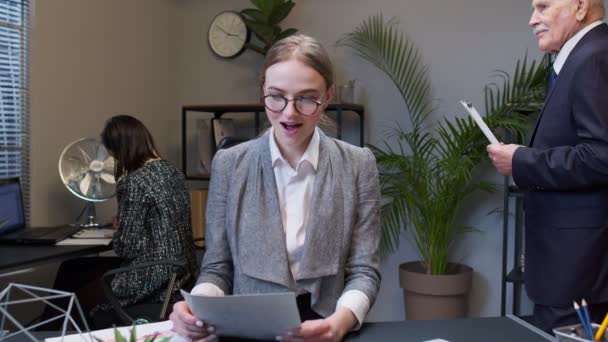 Joven impactada contable mujer de negocios leyendo documentos analizando documentos financieros levantando manos — Vídeo de stock