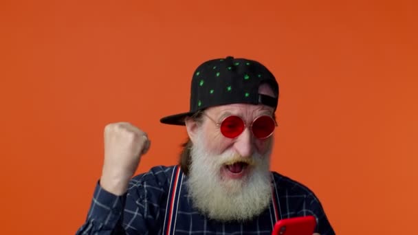 Idős szakállas férfi használja mobiltelefon böngészés online mondani wow igen, nagy győzelem hírek csinál győztes gesztus — Stock videók
