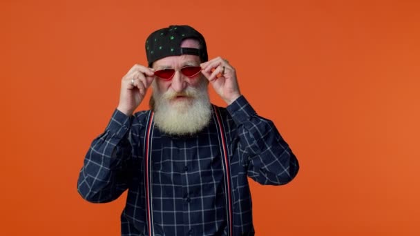 Homme barbu âgé heureux ludique dans les lunettes de soleil et le chapeau oeil clignotant, regardant la caméra avec le sourire — Video