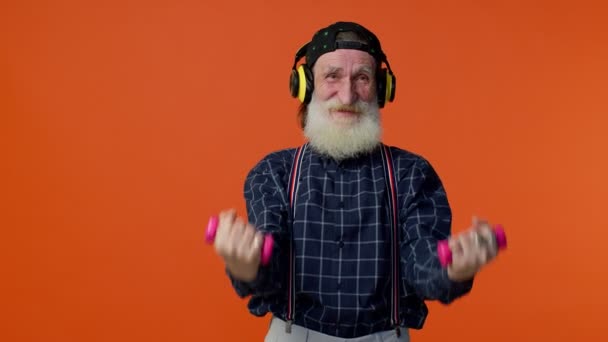 Älterer bärtiger Mann hört Musik über Kopfhörer, trainiert, hebt rosa Hanteln, Gesundheitswesen — Stockvideo