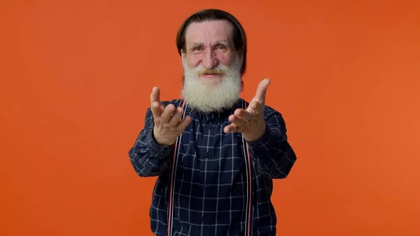 Senior smiling old man with gray-haired looking at camera, fixing beard posing on orange background — Stock Photo, Image