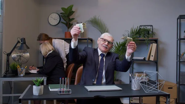 Anciano hombre jefe celebrando éxito de negocios bailando con dinero en efectivo en efectivo en la moderna sala de oficina —  Fotos de Stock