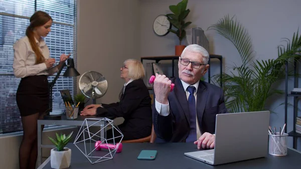 Business man making fitness dumbbells exercises after hard work while sits at office desk workplace — Stock Photo, Image