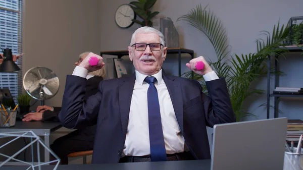 Business man making fitness dumbbells exercises after hard work while sits at office desk workplace