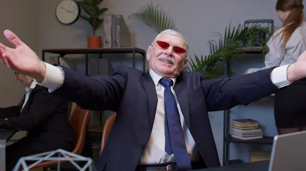 Senior old businessman dancing celebrating sudden victory wearing sunglasses waiting for vacation