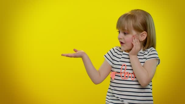 Petite fille enfant montrant les pouces vers le haut et pointant à gauche sur l'espace vide sur fond jaune — Video