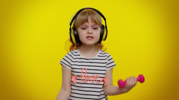 Barnflicka lyssna musik via hörlurar, träna pumpa upp armmusklerna lyfta rosa hantlar — Stockvideo