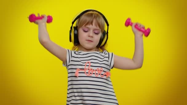 Barnflicka lyssna musik via hörlurar, träna pumpa upp armmusklerna lyfta rosa hantlar — Stockvideo