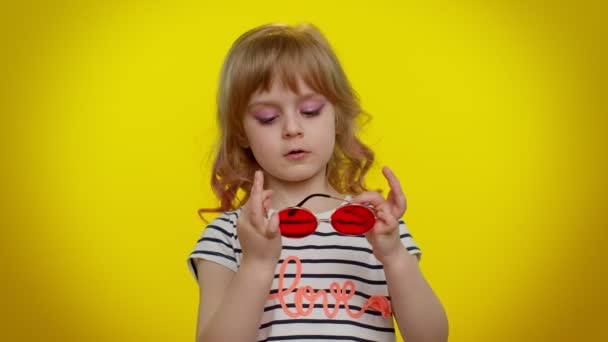 Retrato de divertida niña rubia juguetona en camiseta a rayas con gafas de sol, sonrisa encantadora — Vídeos de Stock