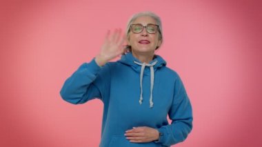 Mutlu, dost canlısı, yaşlı bir kadın elini sallayarak olumlu duygular besliyor.