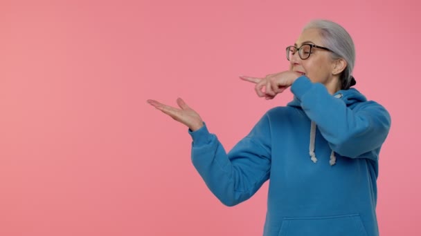 Anciana anciana abuela mostrando pulgares hacia arriba y apuntando a la izquierda en el espacio en blanco, logotipo de la publicidad — Vídeos de Stock