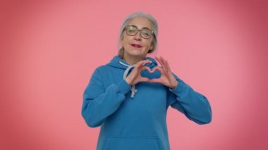Gülümseyen yaşlı kadın kalp hareketi yapar. Aşk işareti iyi duygular ve sempati gösterir.