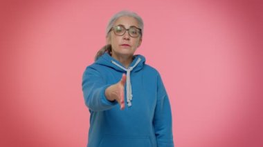 Dost canlısı, kıdemli bir kadın kameraya uzanmış, el sıkışmayı teklif ediyor, nazik bir gülümsemeyle selamlıyor.