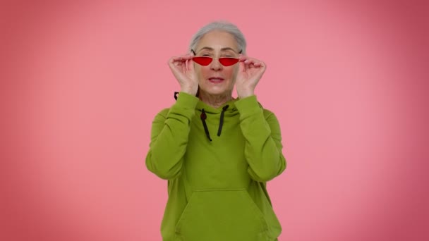 Boldog játékos idős, stílusos nagymama napszemüvegben pislogó szemmel, mosolyogva néz a kamerába — Stock videók