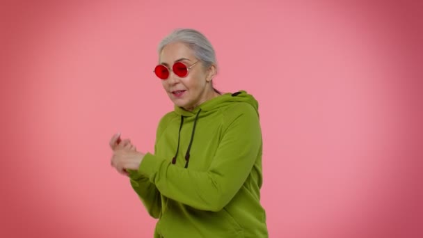 Güneş gözlüklü yaşlı büyükanne kadın müzik dinliyor, gülümsüyor, müzik eşliğinde dans ediyor, eğleniyor. — Stok video